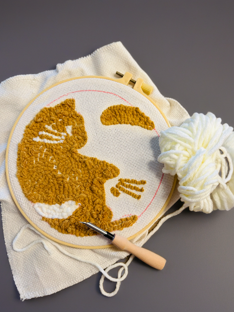 Een borduurring met een half klaar punch needle project van poezen, de naald en een bolletje wol